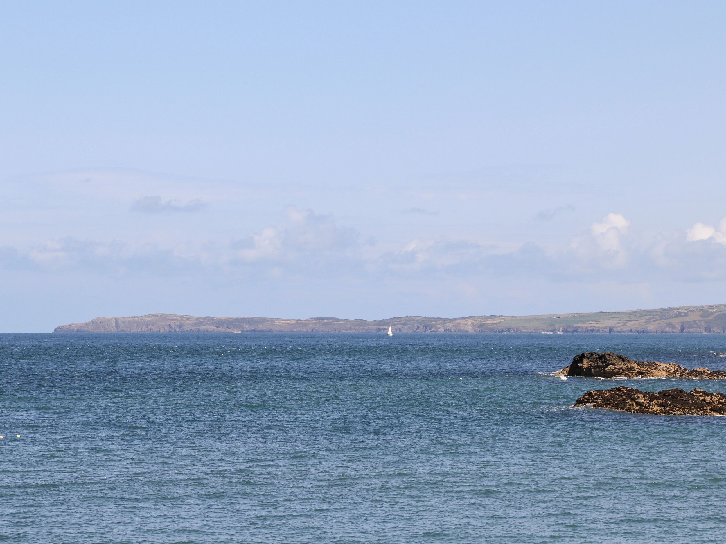 A coastal scene with calm waters, rocky outcrops, and distant cliffs under a clear sky.