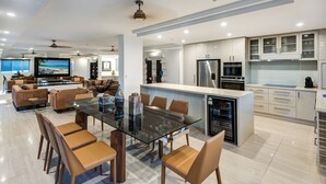 Een moderne keuken met roestvrijstalen apparatuur, een eethoek met een glazen tafel, en een woonkamer met een grote televisie en zachte zitplaatsen.