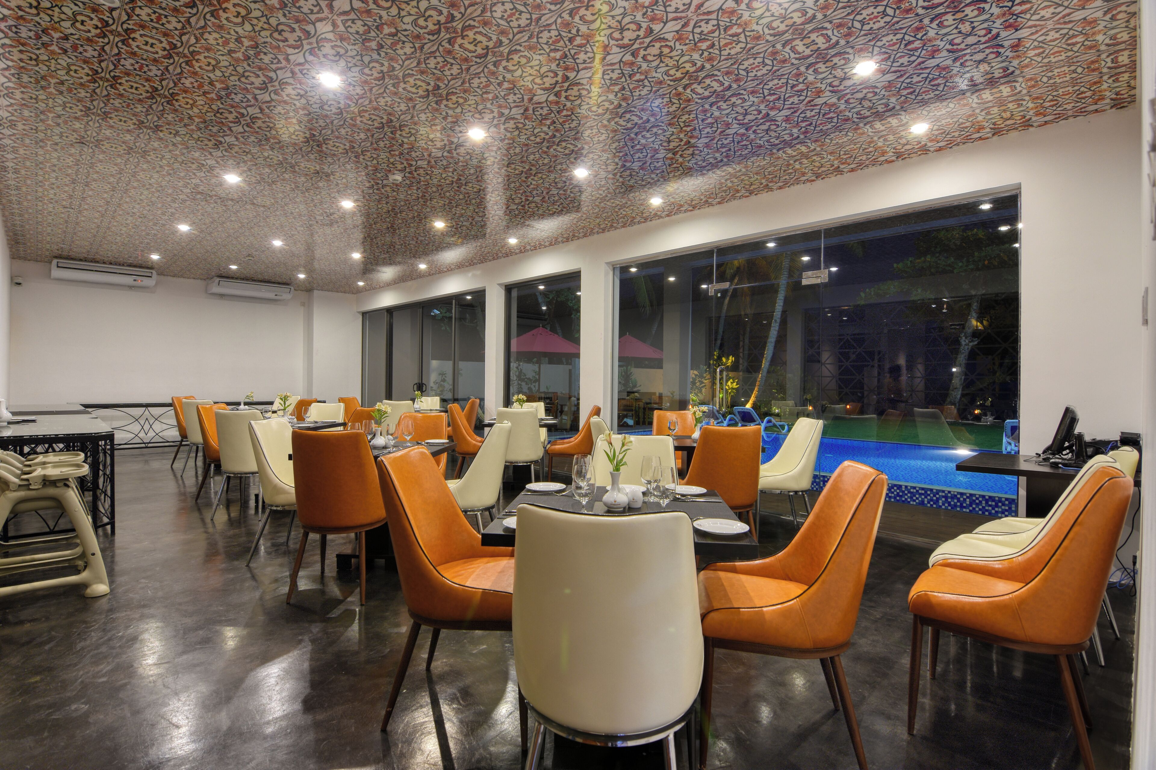 Ein Restaurant mit Blick auf einen Pool, modernen Stühlen und einer gemusterten Decke.