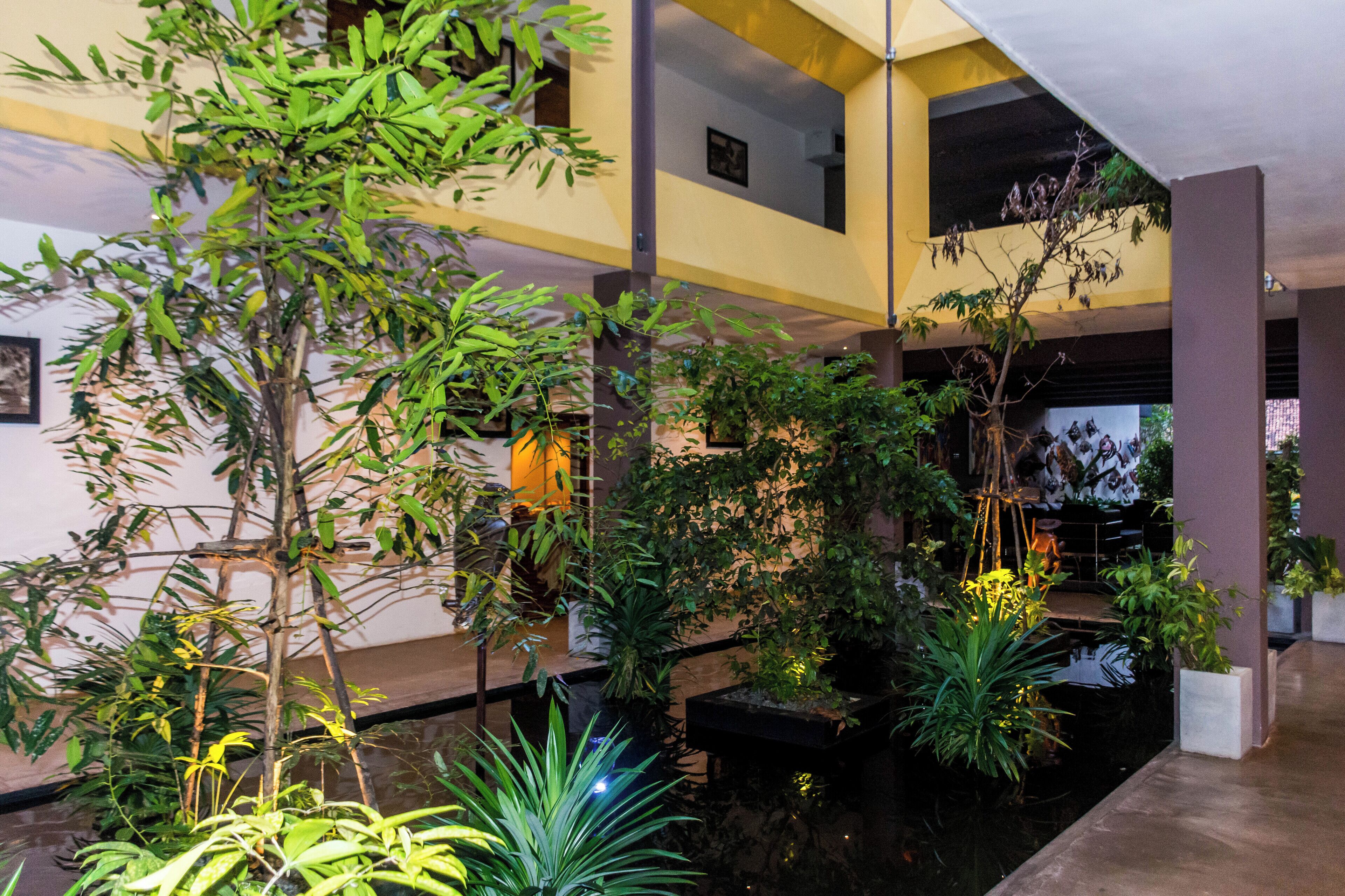 Un atrium intérieur moderne à plusieurs niveaux, agrémenté d’une fontaine centrale et de diverses plantes d’intérieur.