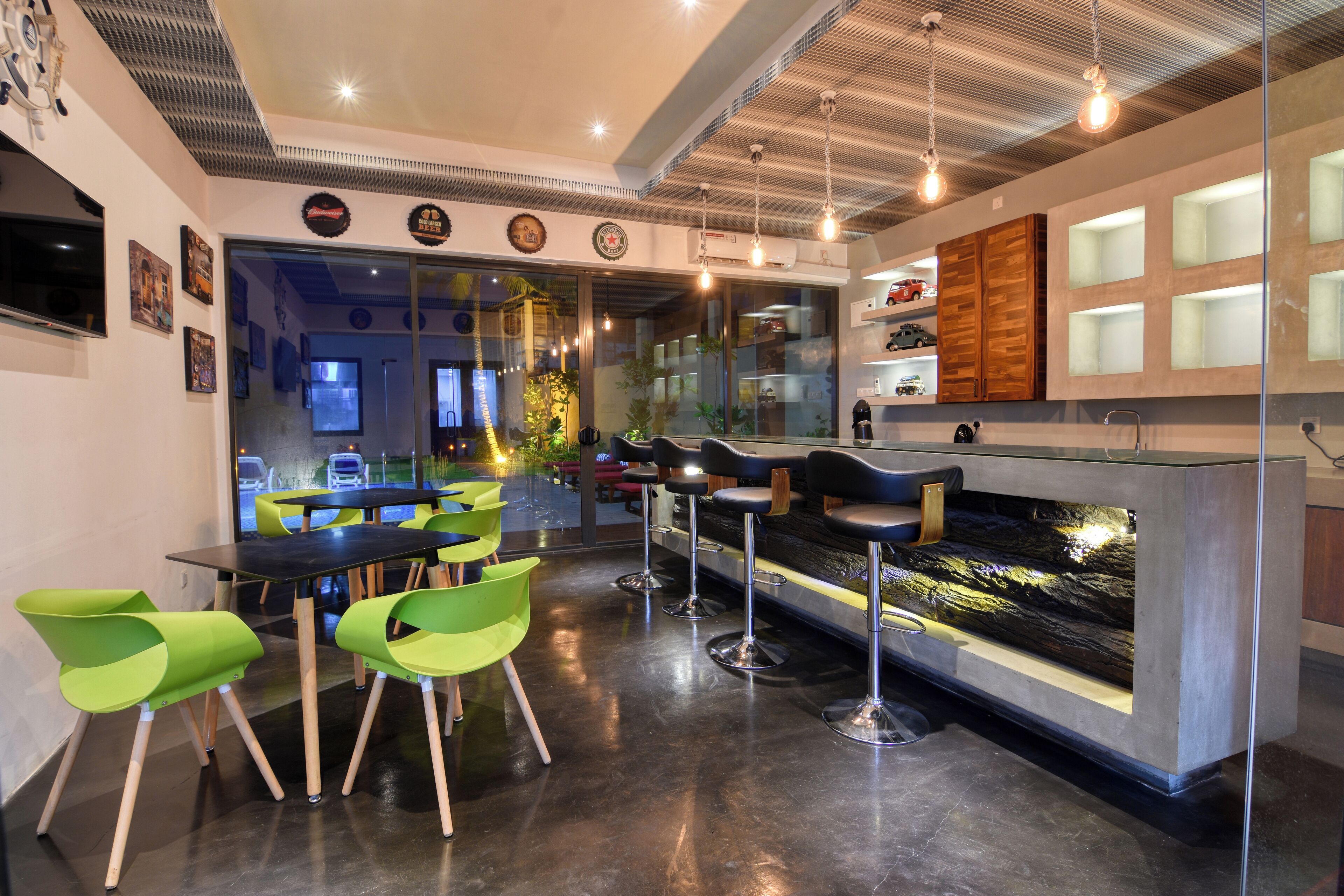 A modern bar area with green chairs, a bar counter, and a large window overlooking the street.