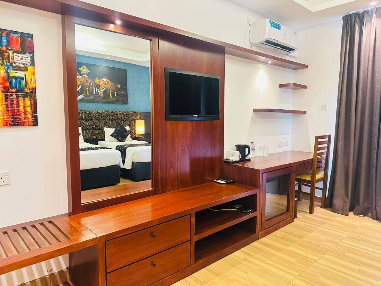 Een hotelkamer met een houten bureau, een flatscreen televisie, een bed met hoofdeinde en een schilderij aan de muur.