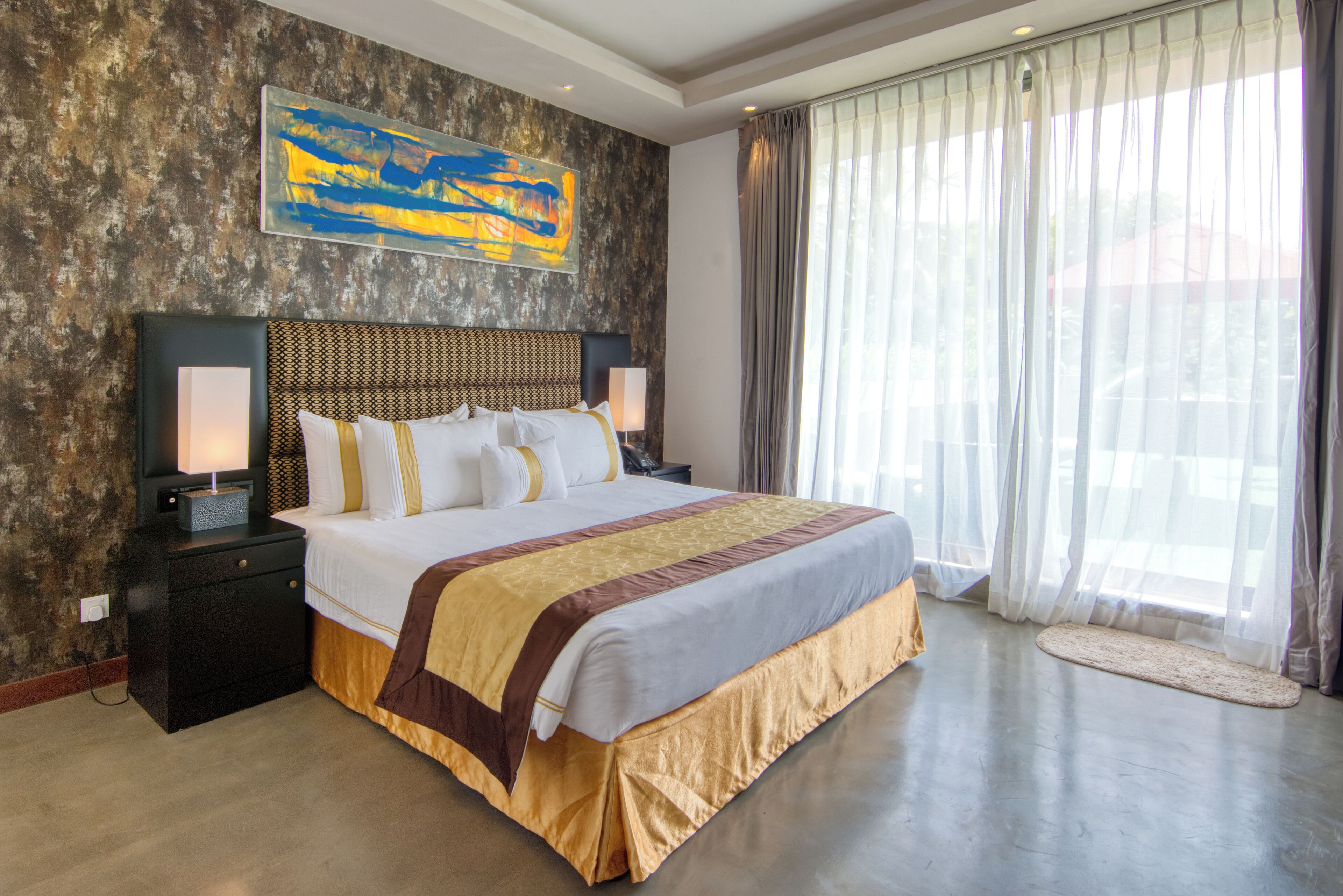A large bed with a headboard, bedside tables, and a painting on the wall.
