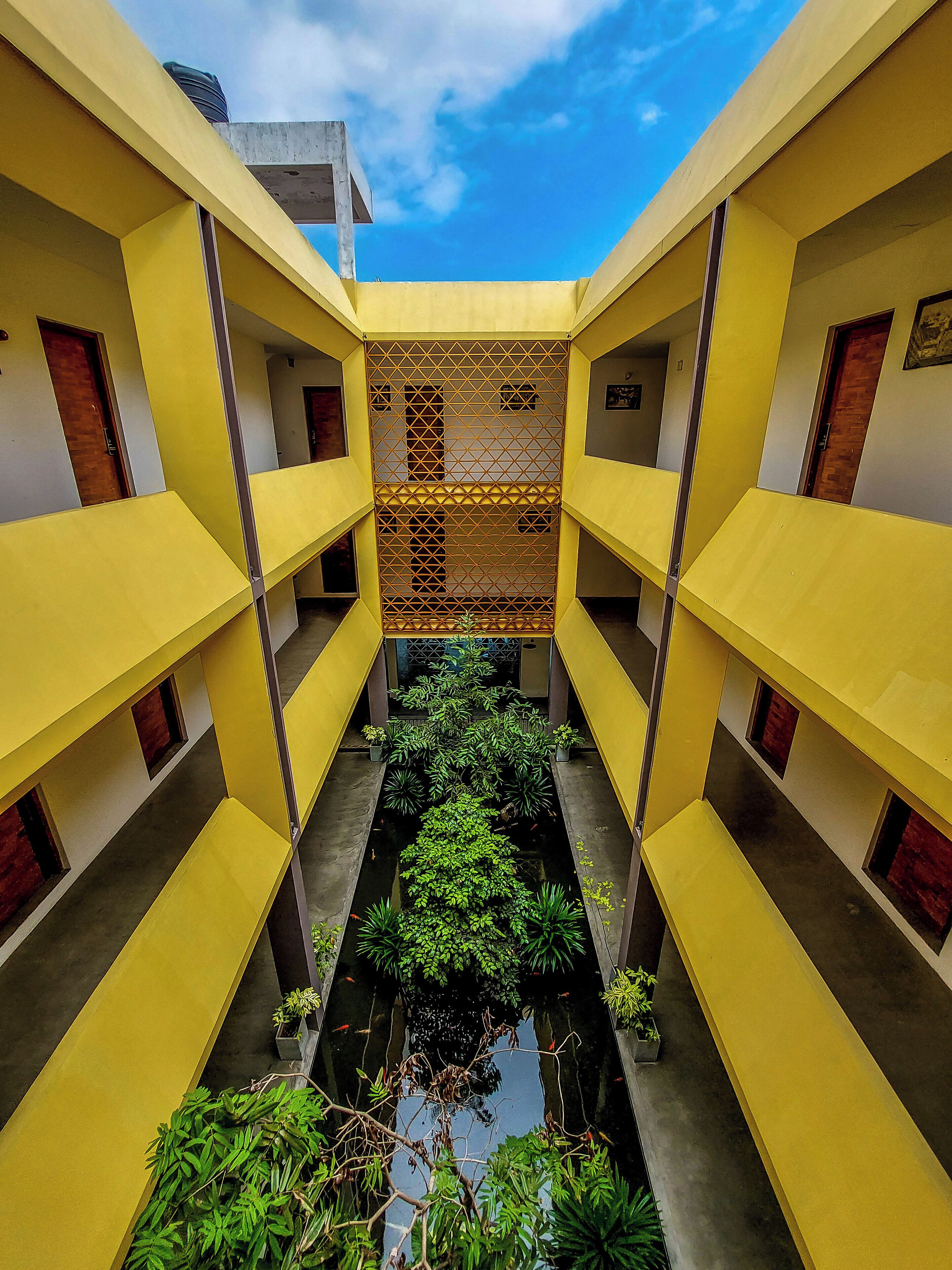 A yellow building with a central water feature and plants.