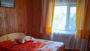 Una habitación con paneles de madera, una cama, una ventana con cortinas y un radiador.
