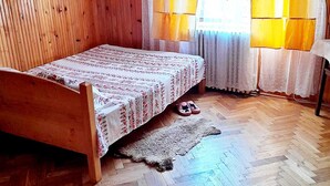 Una habitación con paneles de madera, una cama, una ventana con cortinas amarillas y un tapete en el suelo.