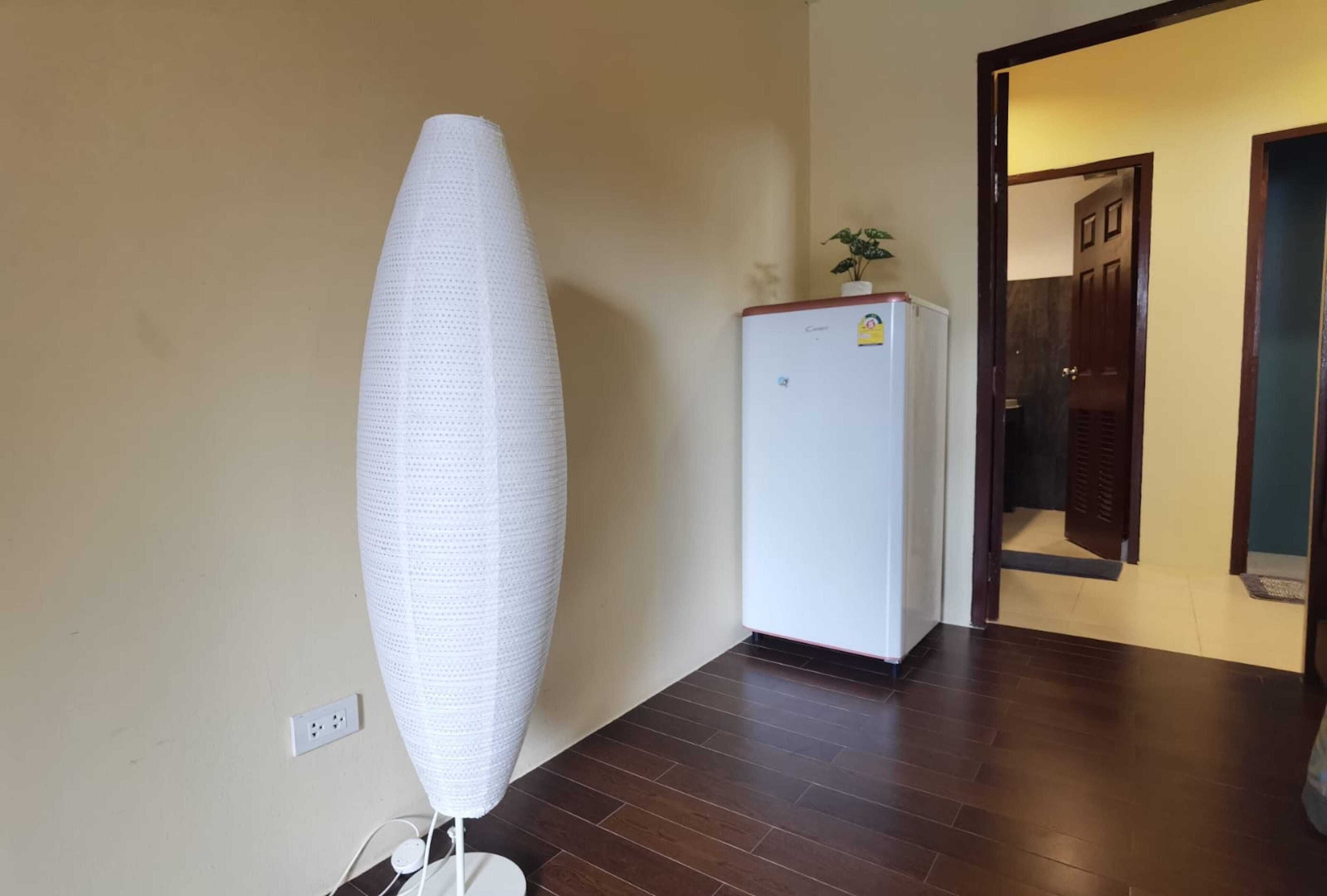 A room with a white, textured sculpture on the wall, a white refrigerator, and a wooden floor.