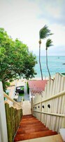 Una escalera de madera que conduce a una zona de playa con vista al océano y palmeras.