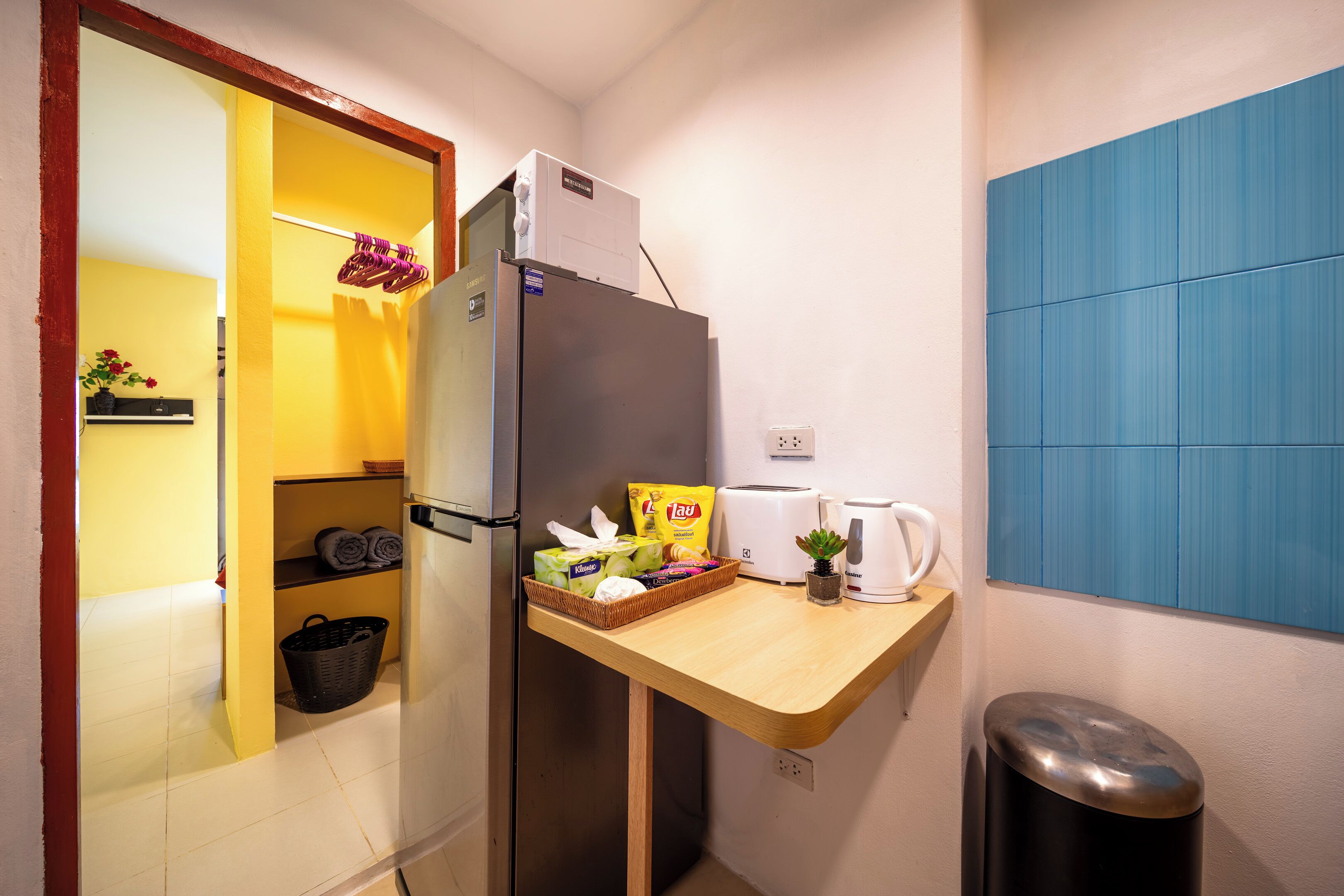 A compact kitchen with a refrigerator, a toaster, a kettle, and a small potted plant on the counter.