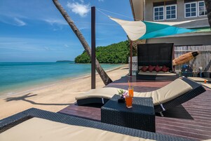 Un salón junto a la playa con mobiliario de mimbre, una mesa con una bebida y vistas al océano.