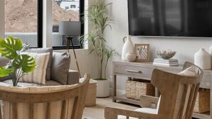 A modern living room with a large TV, comfortable seating, and a view of a desert landscape. - The Solace at Desert Color (by Ember Stays) (St. George)