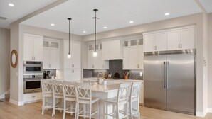 A modern kitchen with white cabinetry, stainless steel appliances, and a central island with bar stools. - The Solace at Desert Color (by Ember Stays) (St. George)