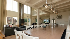 A spacious dining area with a long wooden table, white chairs, and a modern chandelier.