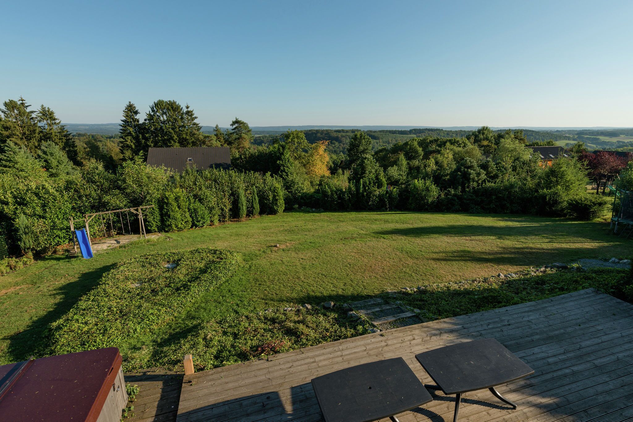 A backyard with a wooden deck, a grassy lawn, and a view of distant trees and hills.