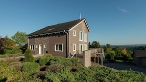 A two-story house with a stone foundation, a wooden deck, and a view of the surrounding landscape.