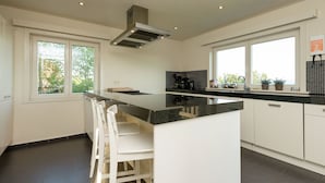 A modern kitchen with white cabinetry, a black countertop, and a central island with bar stools.