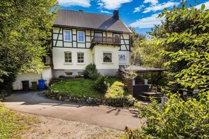 A traditional half-timbered house with a stone pathway leading to the entrance, surrounded by greenery.