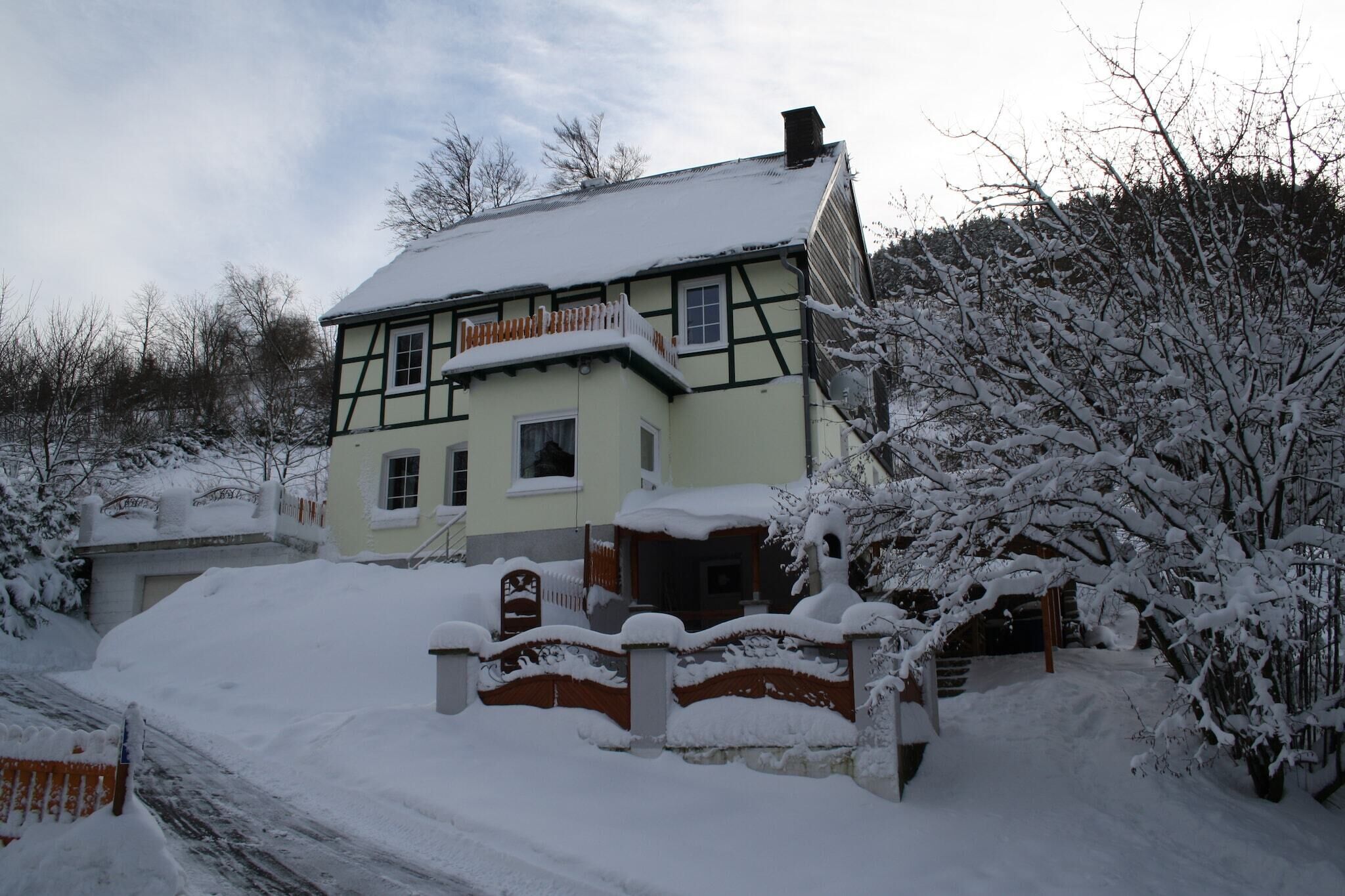 Uma casa tradicional em estilo de enxaimel com telhado coberto de neve e uma pequena varanda.