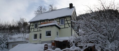 Uma casa tradicional em estilo de enxaimel com telhado coberto de neve e uma pequena varanda.