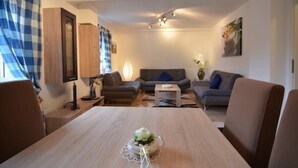 A modern living room with a wooden dining table, grey sofas, and a blue and white checkered curtain. - Chalet im Sauerland nahe Skigebiet Winterberg (Elpe)