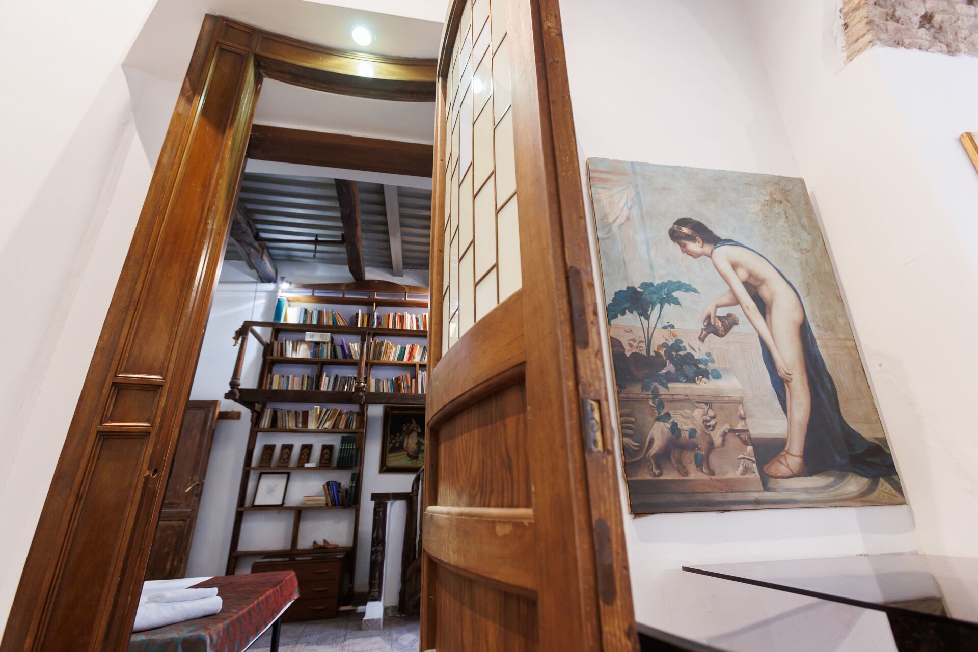 A room with a wooden door, a bookshelf filled with books, and a classical painting on the wall.