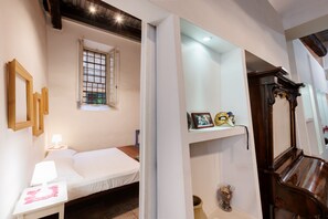 A bedroom with a bed, a nightstand, a window with bars, a shelf with decorative items, and a wooden cabinet. - Your apartment in the heart of Rome (Roma)
