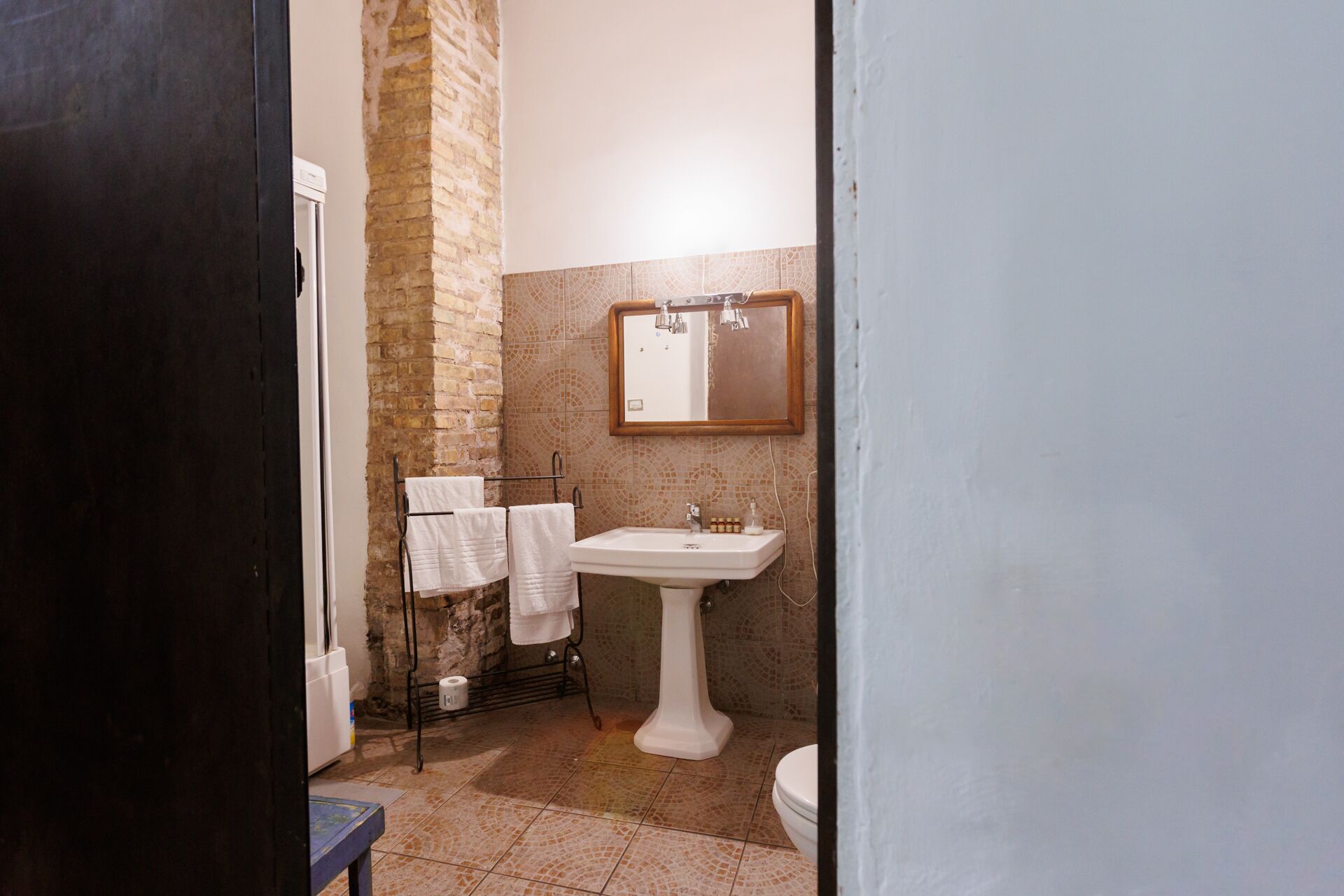 A bathroom with a tiled floor, a white sink, a toilet, and a towel rack with two white towels.