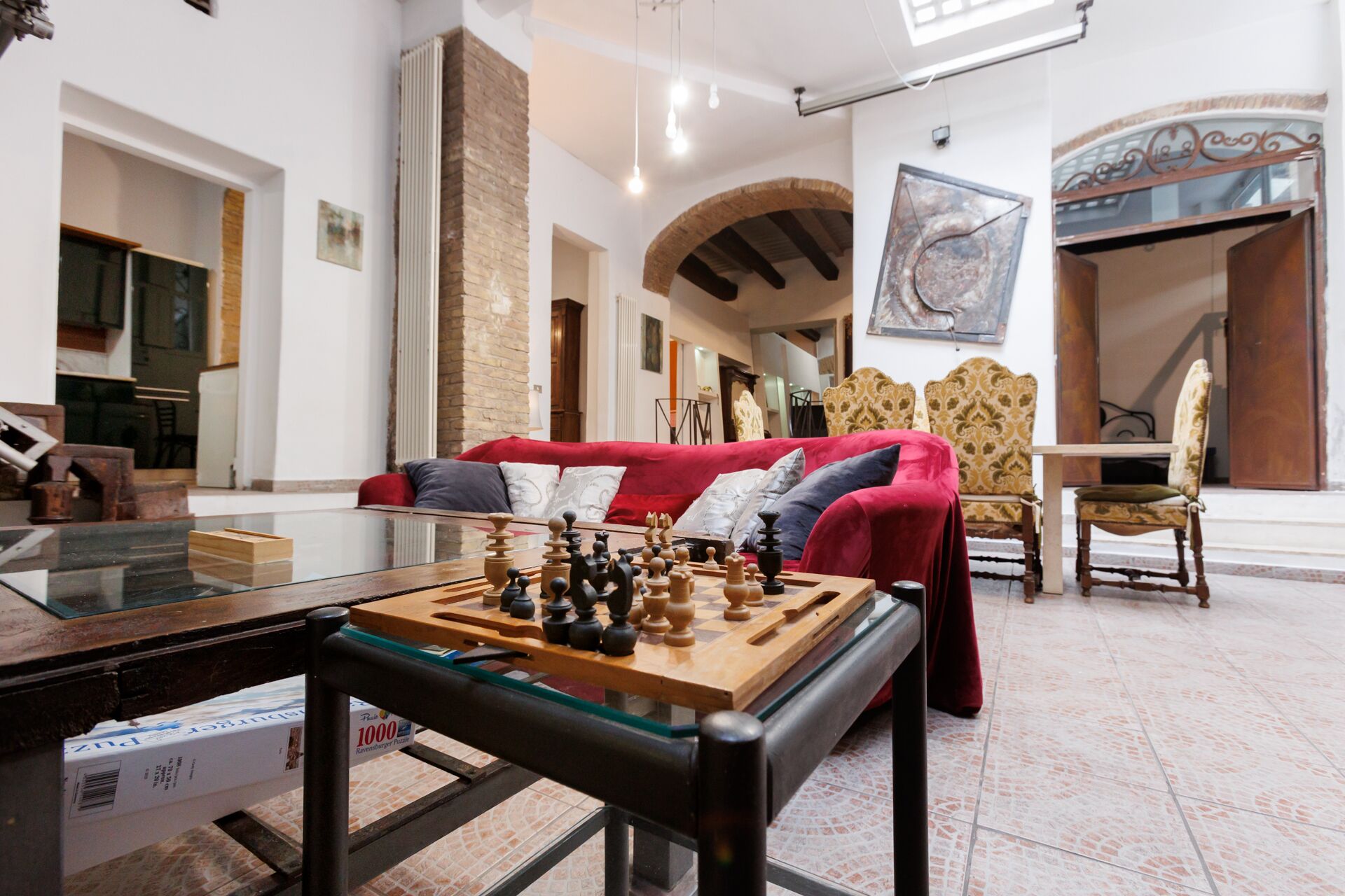 A living room with a chessboard on a glass table, a red sofa, and a patterned armchair.