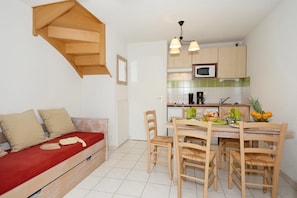 Ett kompakt bostadsutrymme med ett litet kök, en matplats och en soffa med kuddar.