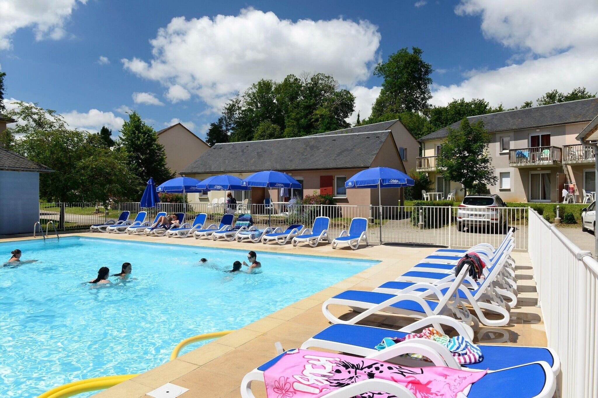 Ein Pool mit Liegestühlen und Sonnenschirmen, umgeben von Gebäuden und Bäumen.