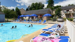 A swimming pool with lounge chairs and umbrellas, surrounded by buildings and trees. - Tranquil Escape with Pool (Rignac)