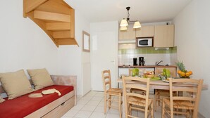 A compact living space with a kitchenette, a dining area with wooden chairs, and a sofa with a red cushion. - Apartment in Rignac near Lake Peyrade (Rignac)