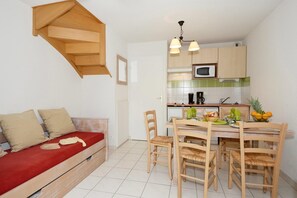 Ett kompakt bostadsutrymme med ett litet kök, en matplats med trästolar och en soffa med en röd kudde.