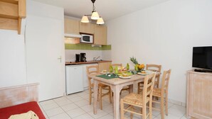 A compact kitchen with a dining table, chairs, and a television. - Apartment in Rignac near Lake Peyrade (Rignac)