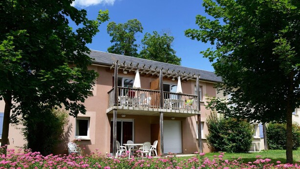 A two-story building with a balcony, outdoor seating, and a garden with pink flowers. - Apartment in Rignac near Lake Peyrade (Rignac)