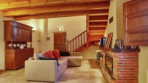 A living room with a fireplace, wooden furniture, and a staircase leading to another level. - Cozy Cottage with Pool & Terrace (Nava)