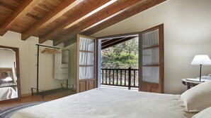 A bedroom with a large bed, wooden ceiling beams, a balcony with a view of trees, and a hanging clothes rack. - Cozy Cottage with Pool & Terrace (Nava)