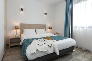A hotel room with a bed, two bedside lamps, a nightstand, a window with curtains, and a wooden floor. - Apartment in La Rochelle near the Beach (La Rochelle)
