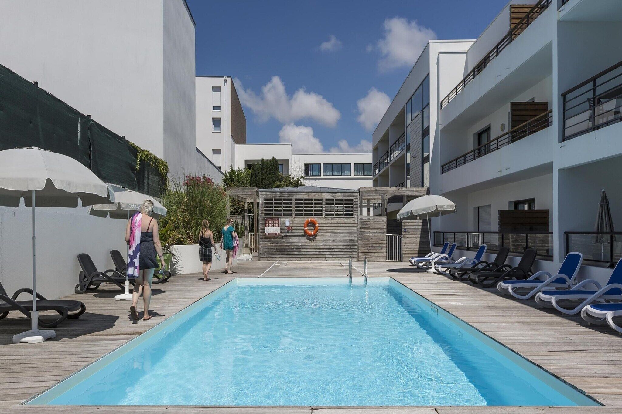 A swimming pool with lounge chairs and umbrellas, surrounded by buildings.