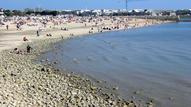 En strand med mennesker, en mobilkran og bygninger i baggrunden.