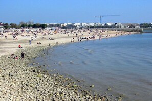 A beach with people, a construction crane, and buildings in the background.