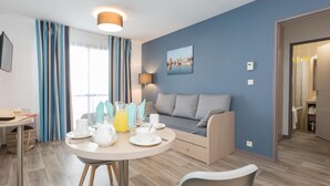 En moderne stue med en sofa, et spisebord dækket med tallerkener, kopper og en kande, samt en lampe.