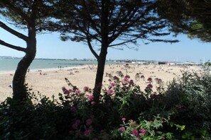 A beach with trees and flowers in the foreground, a sandy beach in the middle, and a pier in the background. - Apartment in La Rochelle near the Beach (La Rochelle)