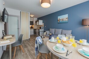 A modern hotel room with a dining area, kitchenette, and a view of the cityscape.