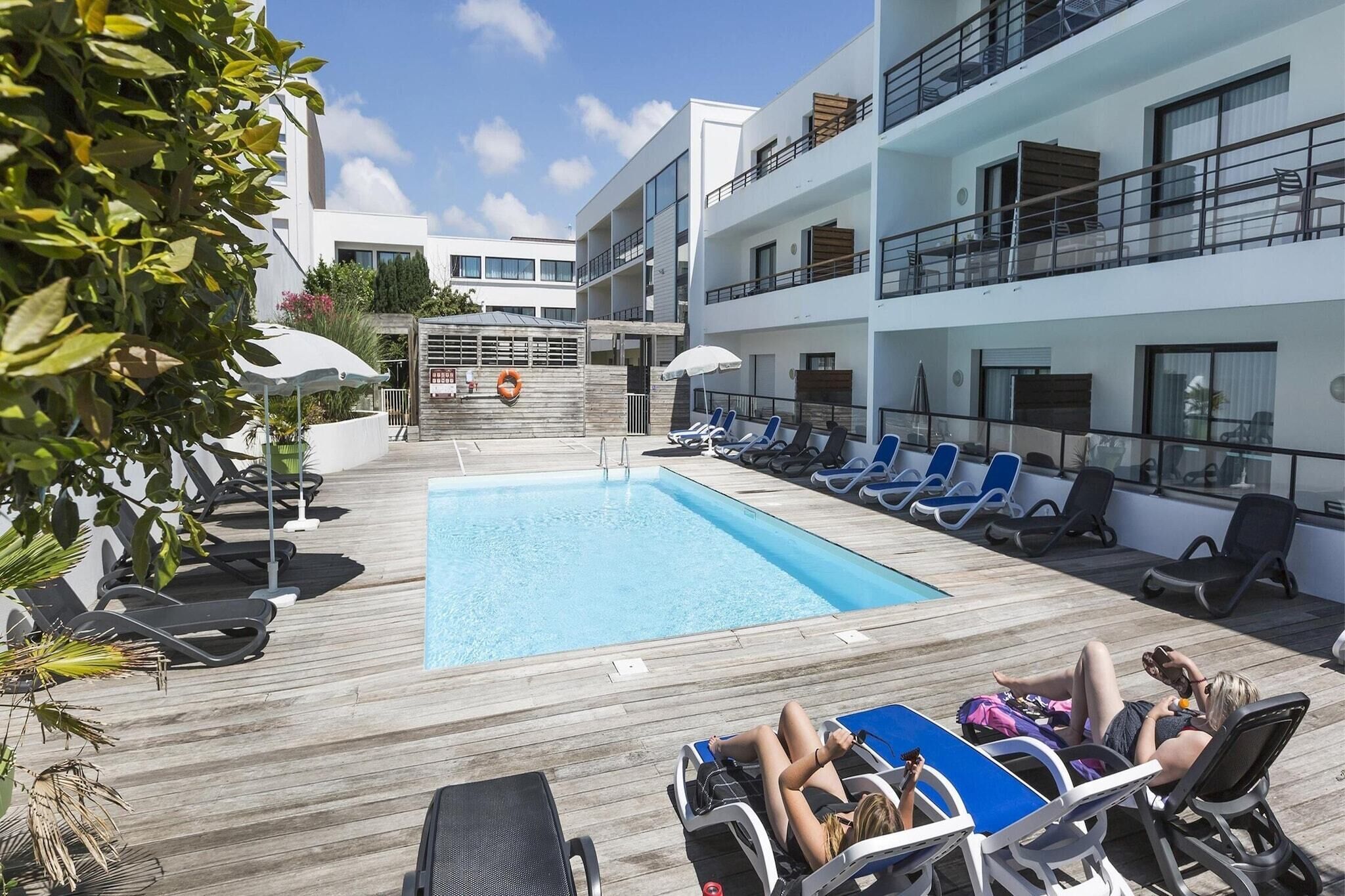 A poolside area with lounge chairs and a swimming pool, surrounded by multi-story buildings.