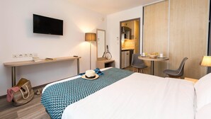 A hotel room with a bed, bedside table, lamp, TV, and a small dining area with chairs and table. - Apartment in La Rochelle near the Beach (La Rochelle)