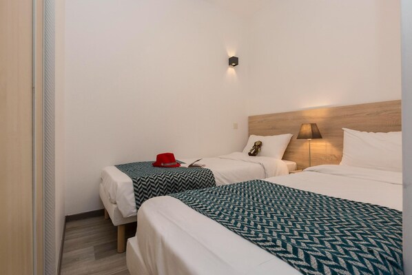 A hotel room with two beds, a nightstand, a lamp, and a wall-mounted light fixture.