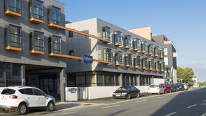 A modern building with a sign for 'Odaly's Vacancies.' There are multiple windows, a parking area, and a street with cars. - Apartment in La Rochelle near the Beach (La Rochelle)