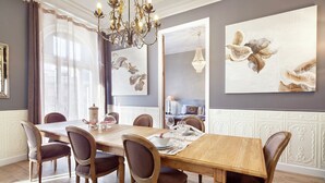 A dining room with a wooden table and chairs, a chandelier, and artwork on the walls.