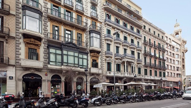 A row of historic buildings with multiple balconies, storefronts including a Starbucks, and a row of parked motorcycles.